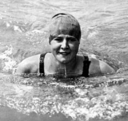 Photographie en noir et blanc de Gertrude Ederle dans l'eau. Sa tête et ses épaules émergent, et elle porte un bonnet de bain.