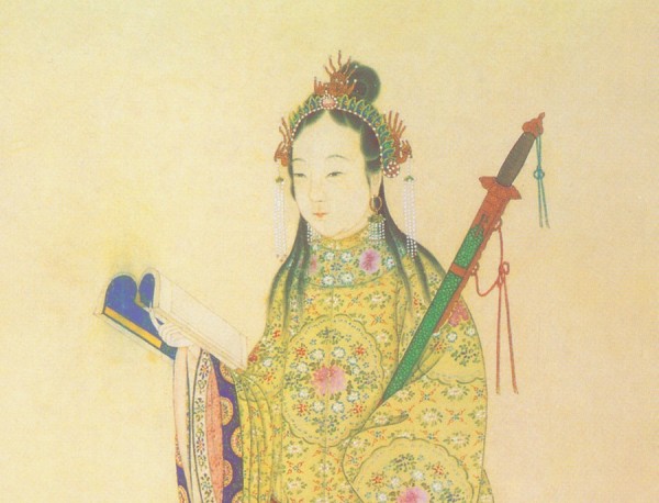 Cette image montre Qin Liangyu. Debout, elle porte une longue tenue chinoise jaune à motif floral et aux manches amples. Elle tient un livre à la main.